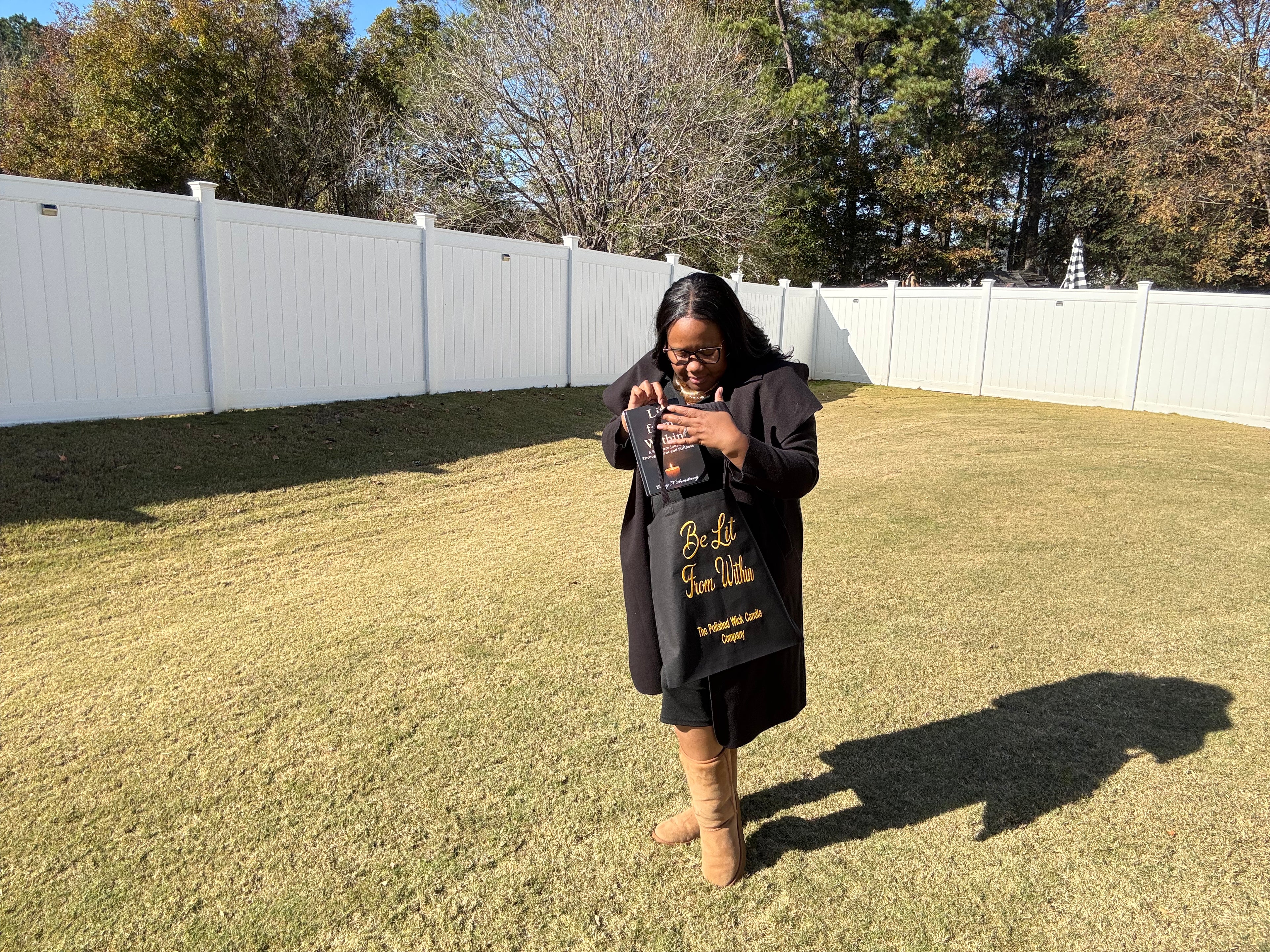 Woman holding a product in a backyard with trees and a white fence in the background