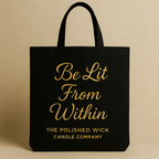 Black tote bag with gold text 'Be Lit From Within' and 'The Polished Wick Candle Company' on a beige background