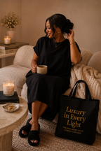 Woman sitting on a couch holding a mug with a candle and 'Luxury in Every Light' bag beside her.