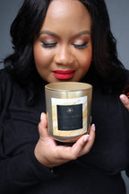 Woman holding a candle with a visible brand label against a neutral background