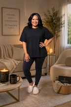 Woman in black outfit standing in a cozy living room with candles and decor.
