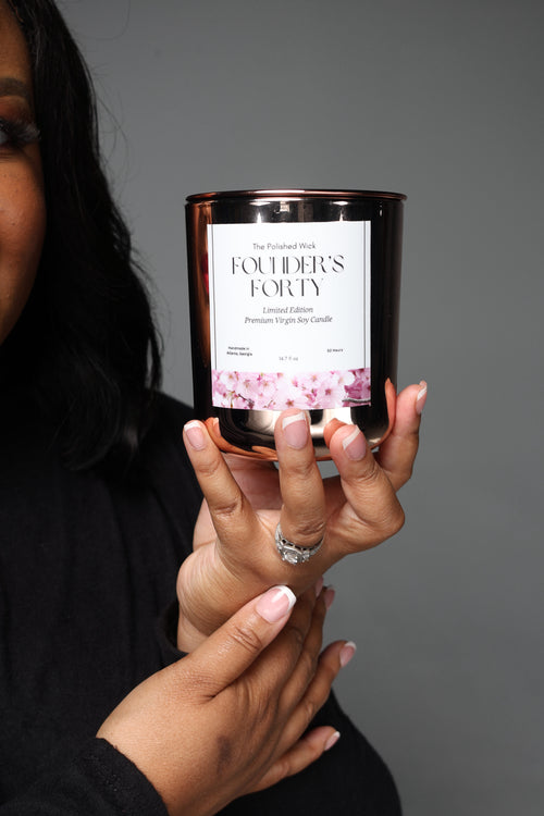 Person holding a candle labeled 'Founder's Forty' against a gray background