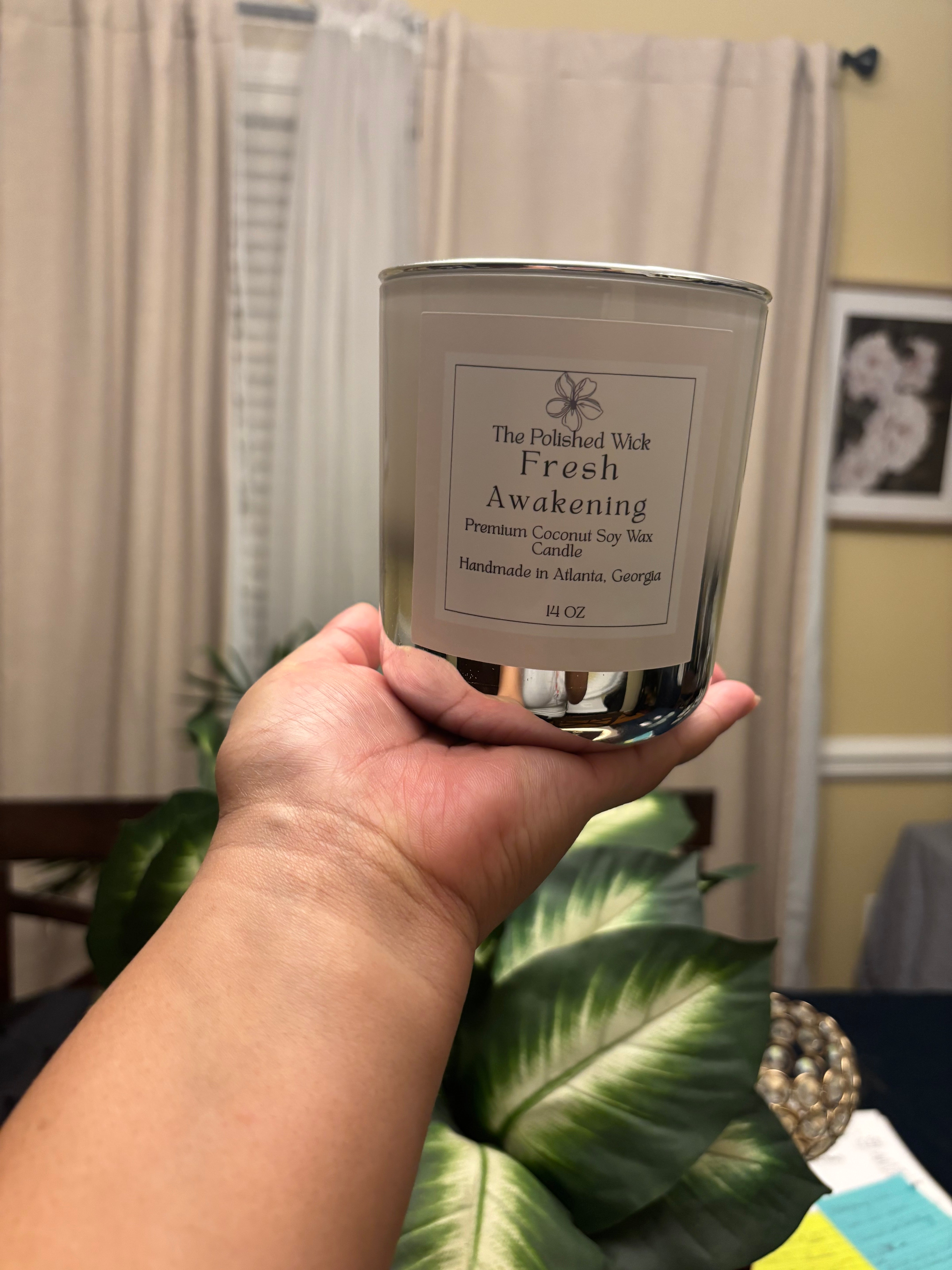 Hand holding a candle labeled 'The Fresh Awakening' with a blurred indoor background