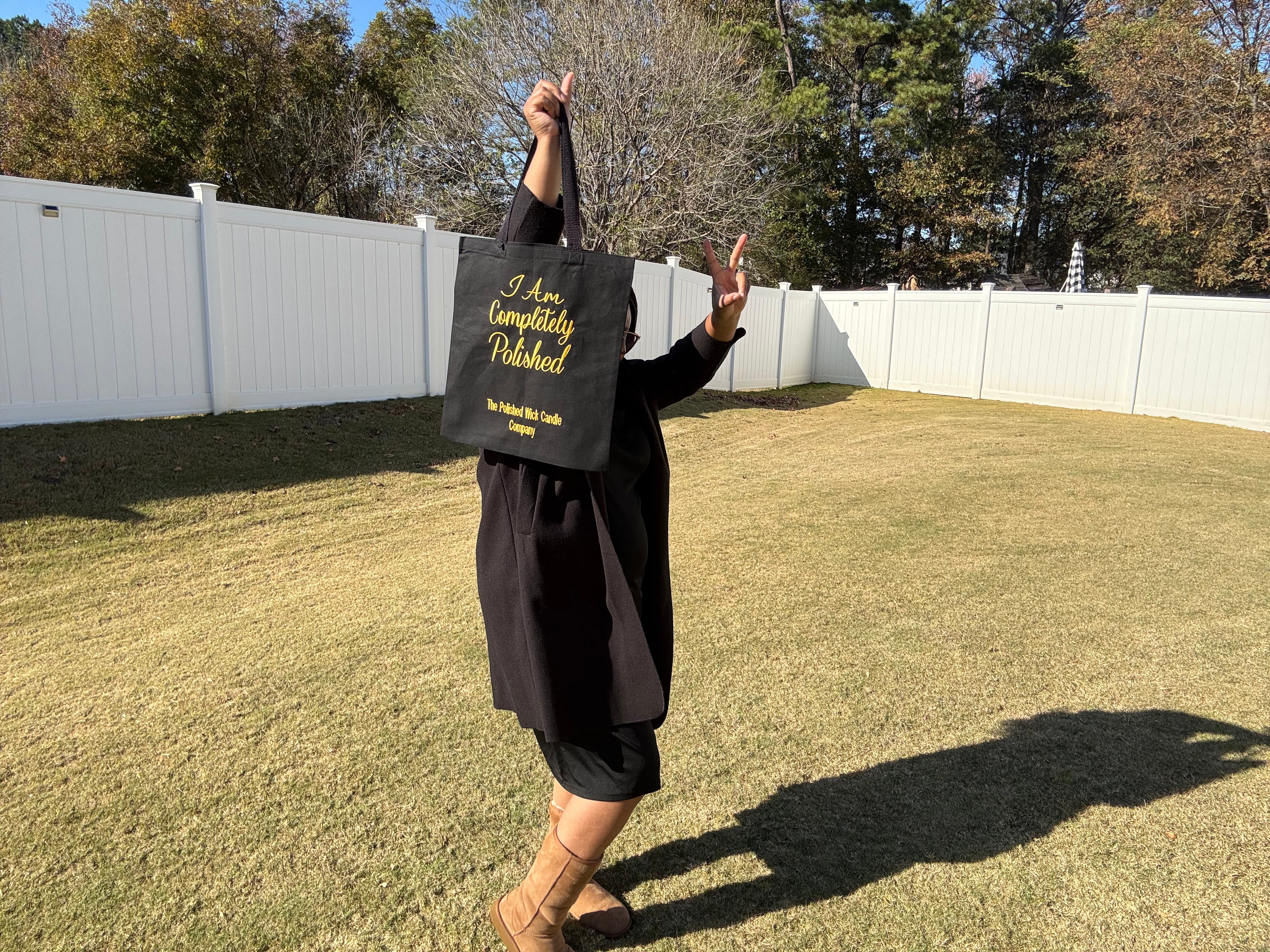 Person in graduation gown holding a black bag with text outdoors.