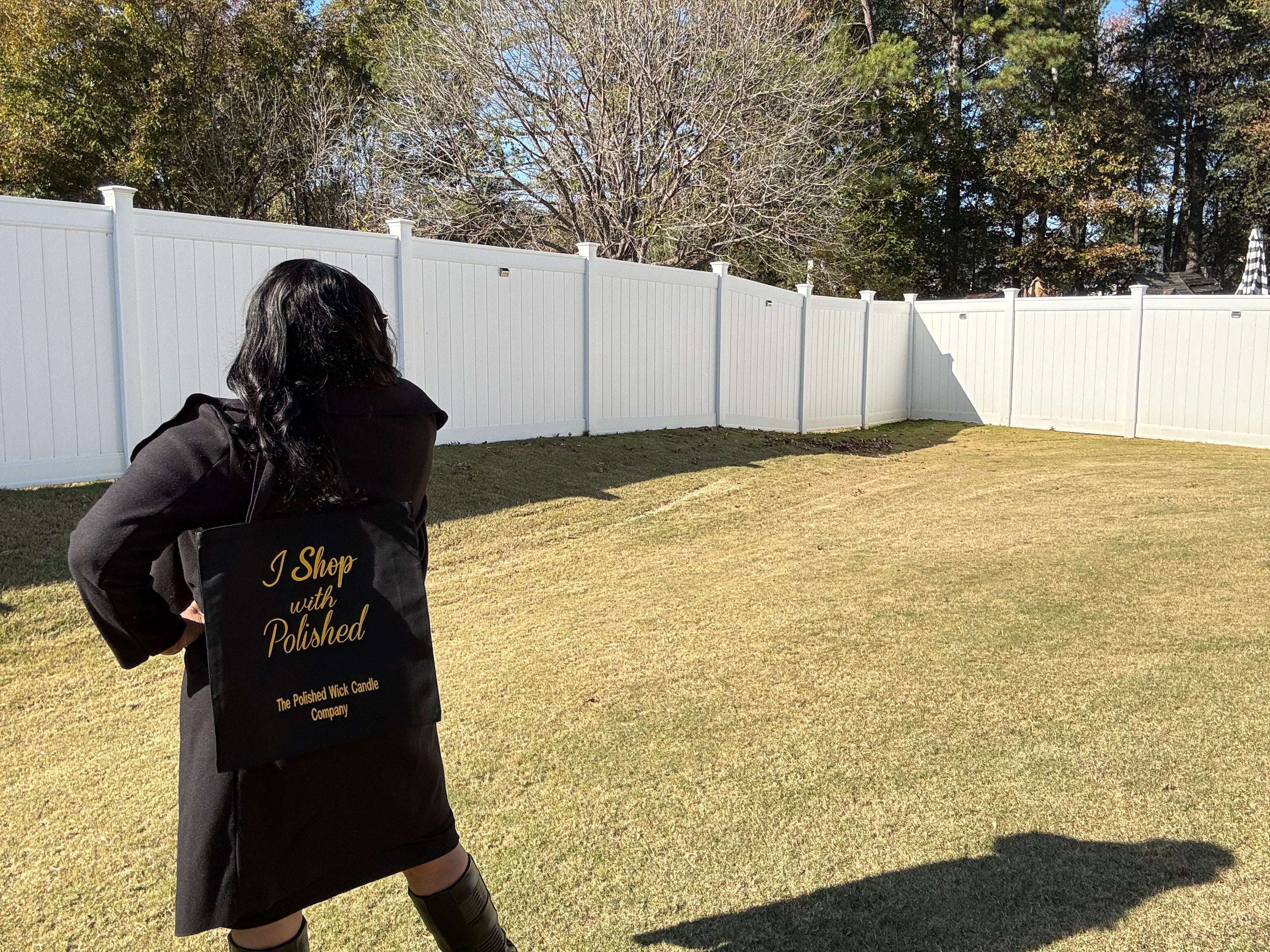 Person wearing a black coat and carrying a black bag with text in a backyard.