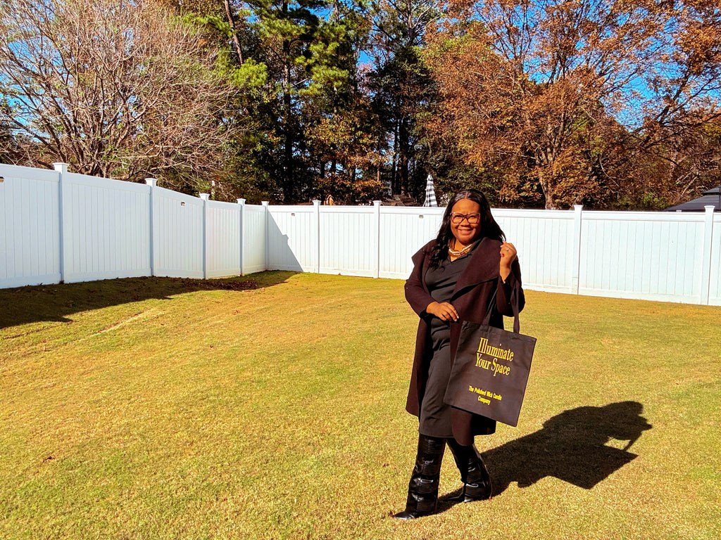 Person holding a luxury black tote bag in a grassy area with trees in the background