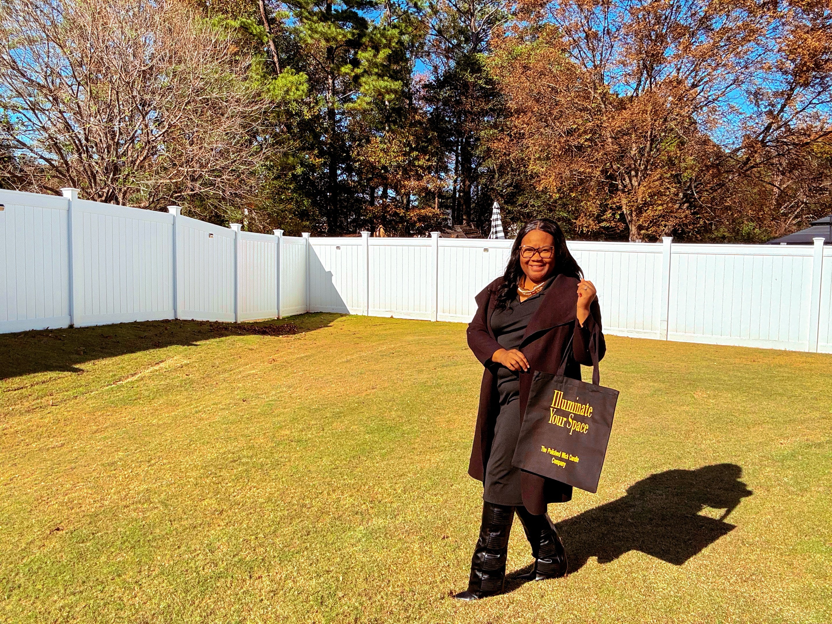 Person holding a luxury black tote bag in a grassy area with trees in the background