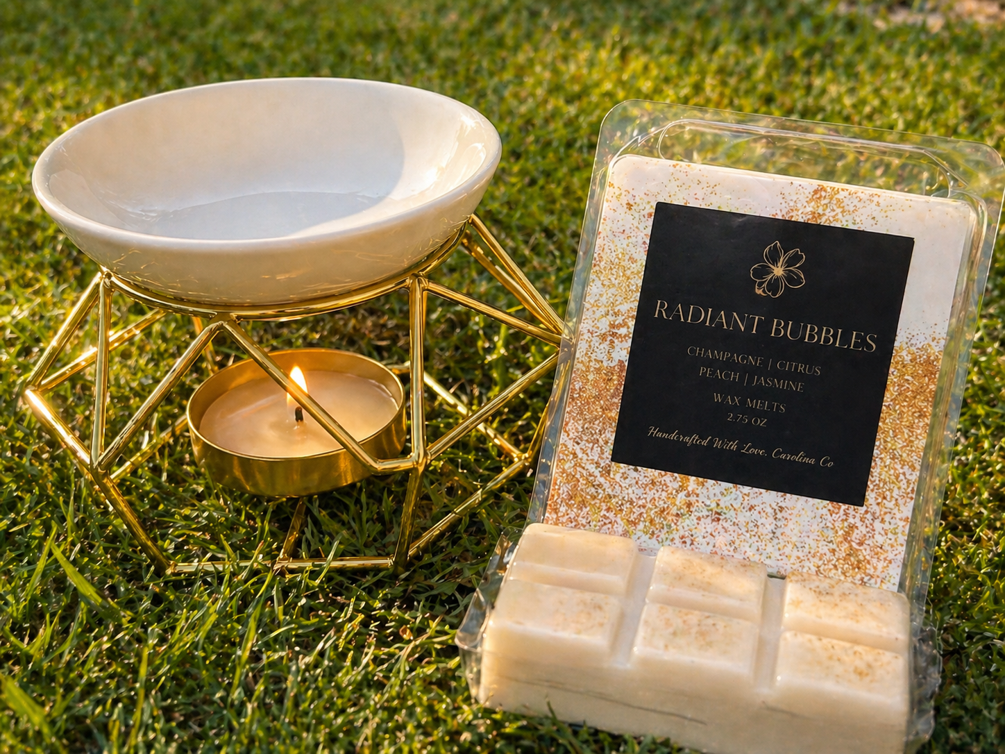Radiant Bubbles wax melts with a lit candle in a decorative holder on grass.