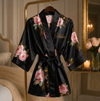 Black satin robe with floral patterns and 'Polisher' text on a hanger in a bedroom setting.