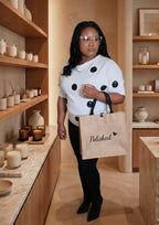 Woman holding a 'Polished' tote bag in a store setting with shelves and decor.