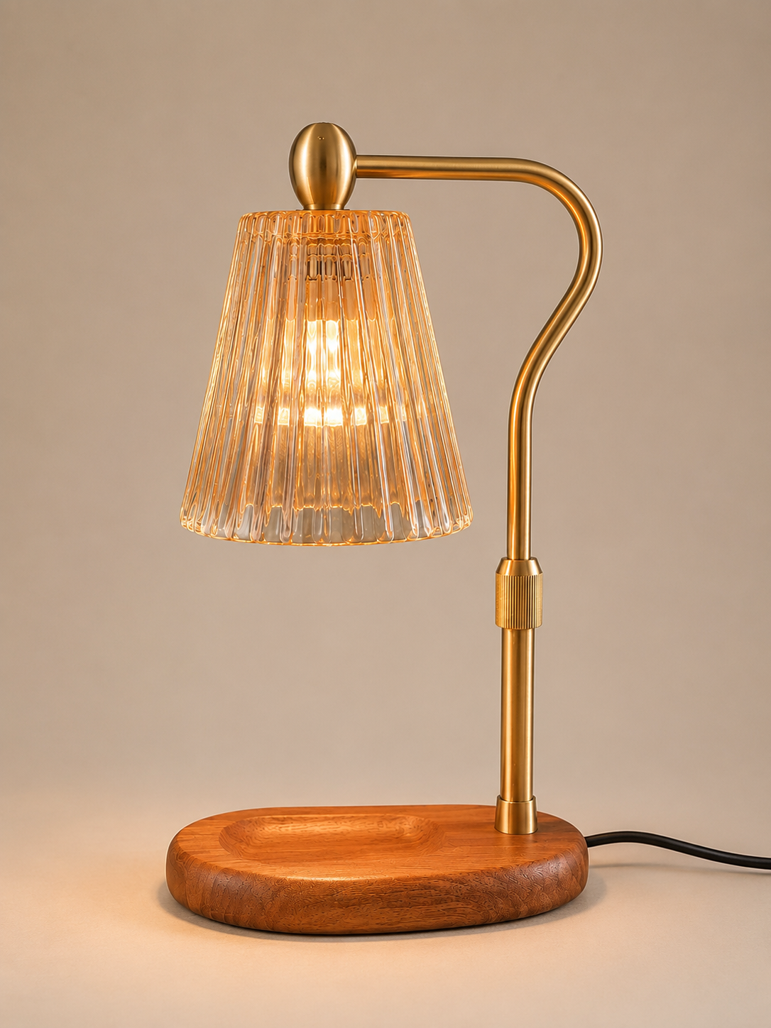 A modern table lamp with a curved brass metal arm, a ribbed clear glass shade, and a round wooden base, shown lit against a neutral beige background.