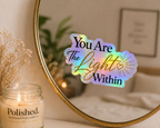 Holographic 'You Are The Light Within' sticker on a mirror with a candle and plant in the background.